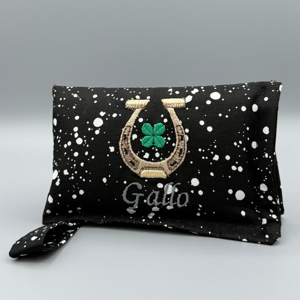 Black and White Speckled horse bit warmer with horseshoe, clover, and Gallo personalization on grey background