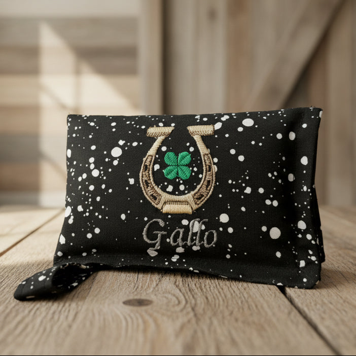 Black and White Speckled horse bit warmer with horseshoe, clover, and Gallo personalization on wooden background