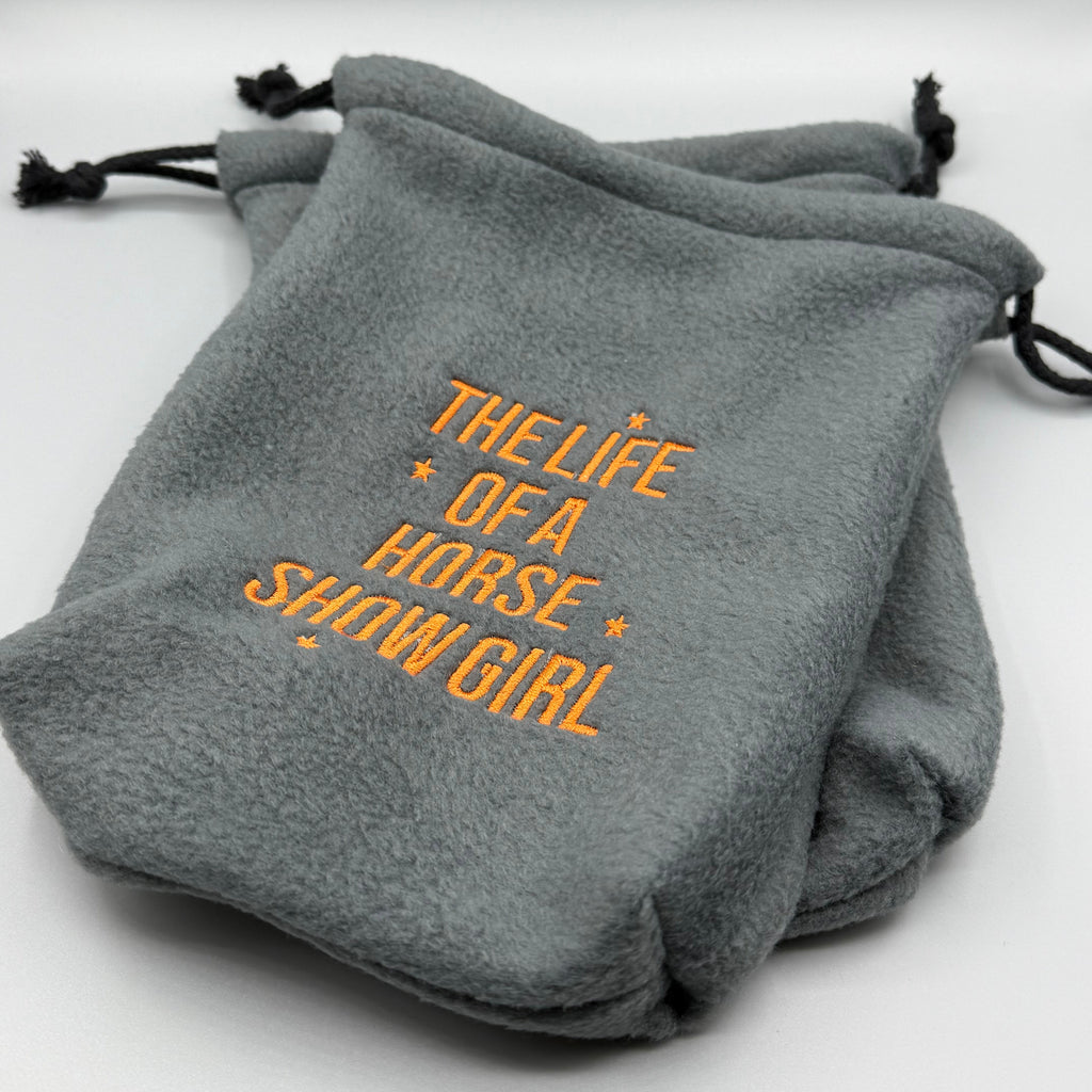 Gray stirrup covers with "The Life of a Horse Show Girl" embroidered in orange thread on gray background. 