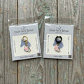 Two little cow charms in Ever So Clever Creations packaging on wood background