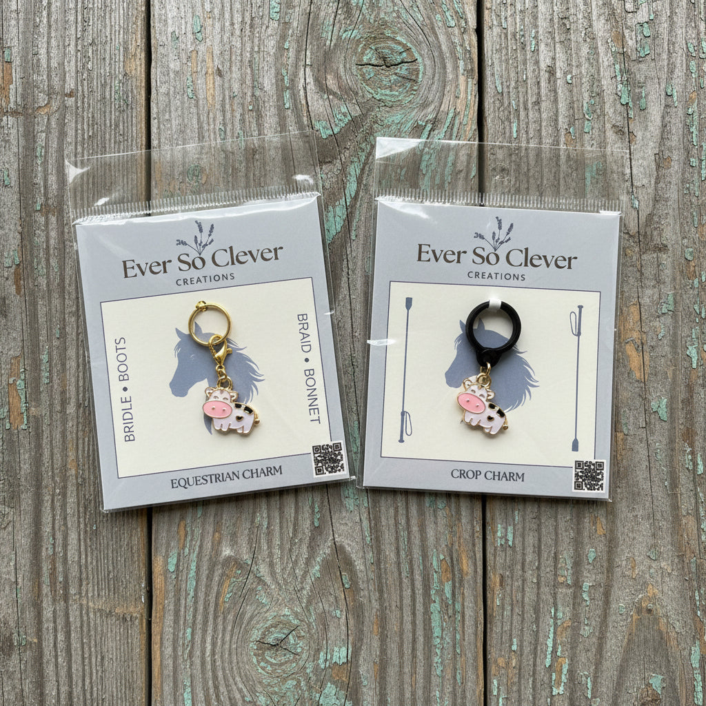 Two little cow charms in Ever So Clever Creations packaging on wood background