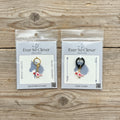 Two love bird charms in Ever So Clever packaging on wood background. 