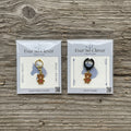 Two packages of Ever So Clever Creations teddy bear charms on a wood background